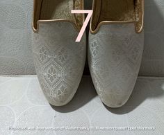 a pair of white shoes with gold trims on the bottom and one has a pink ribbon