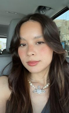 a woman sitting in the back seat of a car wearing a necklace with an anchor on it