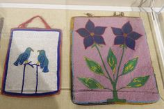 two embroidered bags with flowers and birds on them in a display case, one is pink