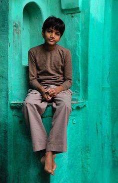 a young boy sitting on the corner of a green wall with his feet propped up