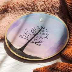 a painted tree on a round wooden frame sitting on a bed next to a teddy bear