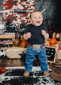 a baby boy standing on top of a rug in front of a cow print wall