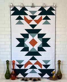 a quilt hanging on the wall next to some vases