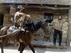 a man riding on the back of a brown horse in front of a brick building