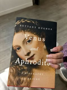 a woman holding up a book about venus and aphrodite in front of her face