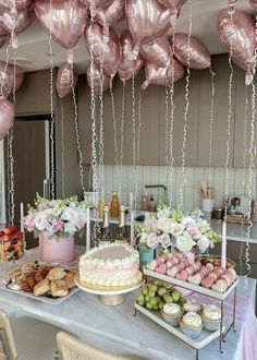 a table topped with lots of cakes and desserts next to balloons hanging from the ceiling