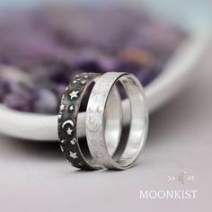 two wedding rings sitting next to each other on top of a purple flower covered table