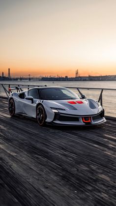 a white sports car driving down a road next to the ocean at sunset or dawn