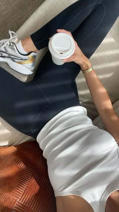 a woman laying on top of a couch holding a coffee cup in her right hand