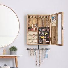 an open wooden jewelry box sitting on top of a white wall next to a mirror