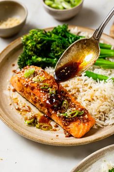 a plate with rice, broccoli and salmon being drizzled with sauce