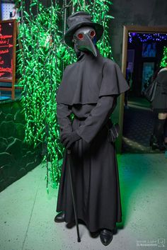 a man dressed in a plague costume and holding a cane standing next to a green wall