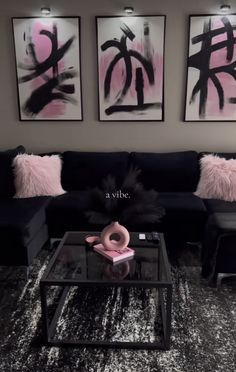 a living room with black couches and pink pillows on top of the coffee table