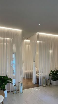 a living room with white drapes and plants in the corner on either side of the window