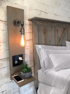 a bed with white sheets and pillows next to a wooden headboard