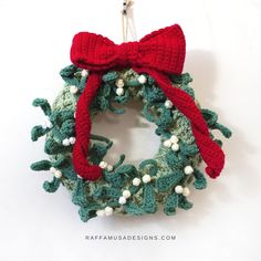 a crocheted christmas wreath hanging from a hook on a white wall with a red bow