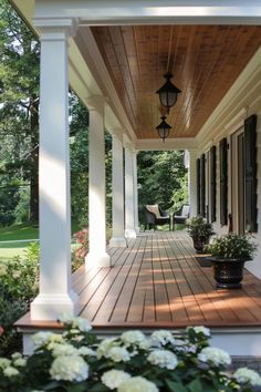 a porch with white flowers on it and a lamp hanging from the side of the house