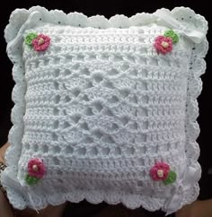 a white crocheted pillow with pink flowers on the front and back, sitting in someone's hand