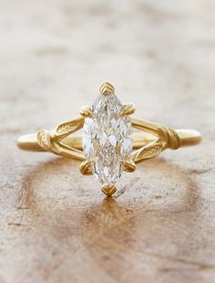 a yellow gold ring with a pear shaped diamond in the center on a wooden surface