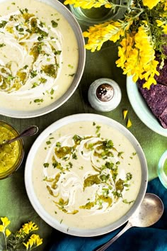 two bowls filled with soup next to yellow flowers and tortilla chips on a table