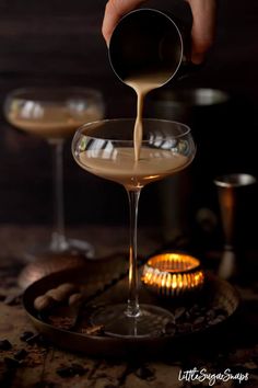 a person pouring some liquid into a glass filled with something brown and white in front of two other glasses