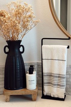 a black vase sitting on top of a counter next to a white towel and bottle