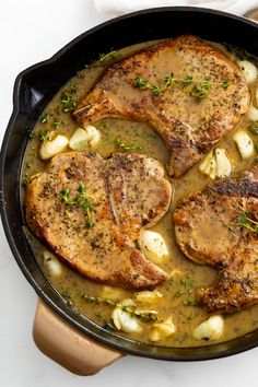 two pork chops with potatoes and gravy in a cast iron skillet