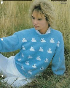 a woman sitting in the grass wearing a blue sweater with white bunny rabbits on it