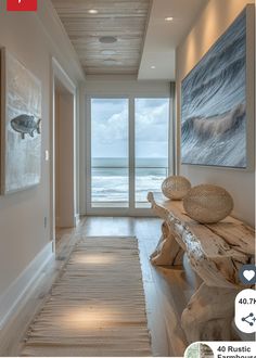 a long hallway leading to the ocean with large windows and artwork on the wall above it