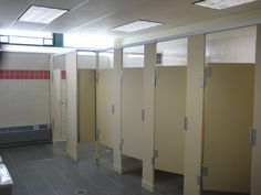 a row of stalls in a public restroom with tiled flooring and walls lined with partitions