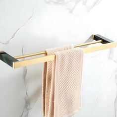 a gold towel rack with two towels hanging on it's sides and a marble wall in the background