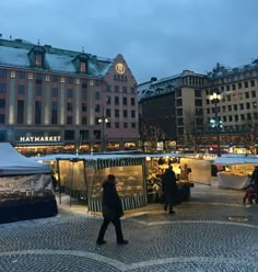 people walking around an open air market in the middle of a city at night time