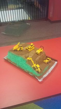 there is a cake shaped like a construction site on the ground with yellow tractors in it