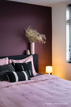 Donkere, auberginekleurige muur in de kleur Brinjal van Farrow & Ball in de slaapkamer. Op het bed ligt een ouderoze linnen dekbedovertrek van H&M. Daarop een aantal zwart wit gekleurde, grafische modderdoek kussens.