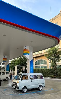 a white van is parked in front of a blue and red gas station with other vehicles