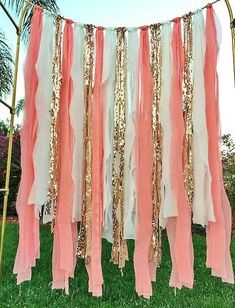 pink, white and gold streamers are hanging from a metal pole in the grass