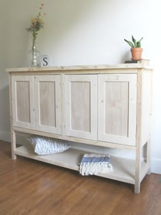 a white wooden cabinet sitting on top of a hard wood floor next to a plant