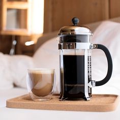 there is a coffee maker next to a cup on the tray in front of the bed