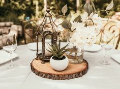 an arrangement of flowers and greenery on a wood slice at a wedding reception table