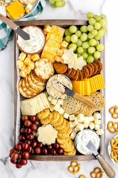 a platter with cheese, crackers, grapes and pretzels