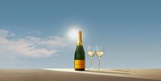 two wine glasses sitting next to a bottle of champagne on top of a sandy beach