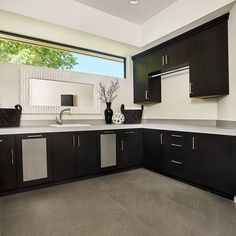 an empty kitchen with black cabinets and white counter tops is seen in this image, there are two vases on the sink