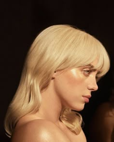 a blonde woman with long hair and no bra looking off to the side in front of a black background