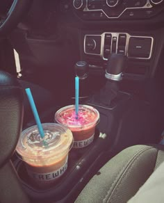 two drinks in plastic cups on the dashboard of a car