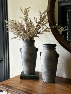 two vases sitting on top of a wooden table next to a mirror with flowers in it