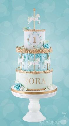 a three tiered cake decorated with blue and white frosting, gold trimmings and a horse on top