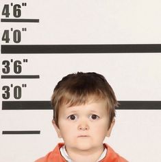 a little boy is in front of a mugshot wall with the height of his body