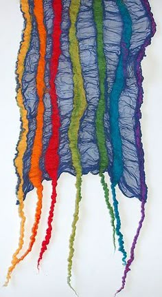 a group of multicolored yarns hanging from the ceiling in front of a white wall