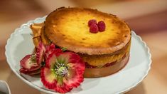 a cake with raspberries on top sits on a plate next to a flower