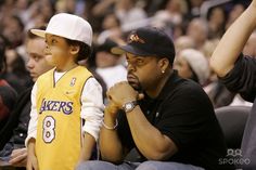 two young men sitting next to each other at a basketball game, one wearing a lakers jersey